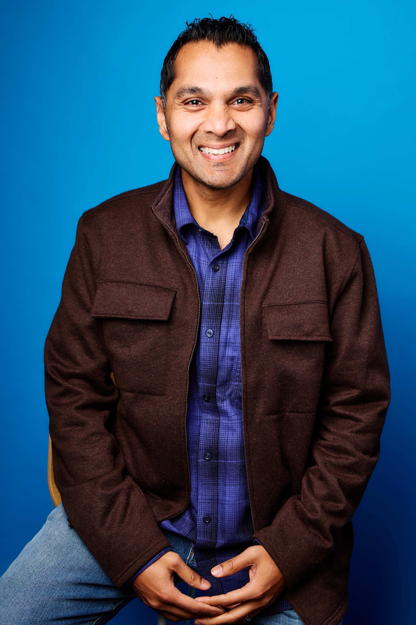 Srini, arms crossed and smiling, against a bright blue studio backdrop